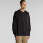 Person in a black sweatshirt and khaki pants standing against a plain background.