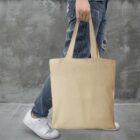 Person holding a beige tote bag, wearing jeans and white sneakers.