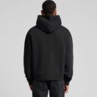 Person in a black hoodie and jeans facing away in a neutral setting.