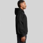 A man in a black hoodie stands in profile against a gray background.