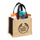 Jute and black bag with The Body Shop logo, filled with colorful toiletries.