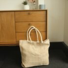 Woven tote bag with white handles in front of a wooden cabinet.
