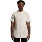 Man in a beige short-sleeve button-up shirt standing against a white background.