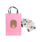 Pink gift bag with a bear design beside scattered colorful stickers.