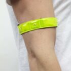 A person wearing a white shirt has a bright yellow reflective band around their upper arm. The band is shiny and is secured with a small button.
