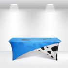 Blue and white table cover with cow print and logo in a spotlighted room.