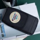 Black pouch with a #Kindness Works Here patch resting on stacked books.