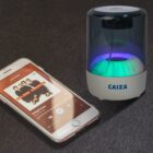 Smartphone with music app and glowing Bluetooth speaker on a dark surface.