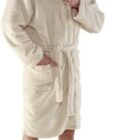 Smiling man wearing a beige bathrobe stands barefoot against a white background.