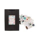 Black gift bag with a floral label, next to assorted decorative stickers.