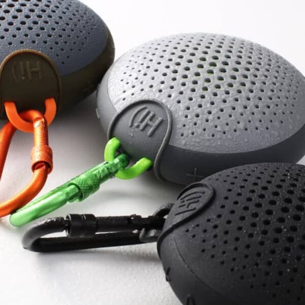 Three round portable speakers in black, gray, and green with carabiners attached.
