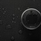 Round black speaker on a wet, glossy surface with water droplets.