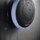 Black waterproof speaker with water droplets on a wet surface.