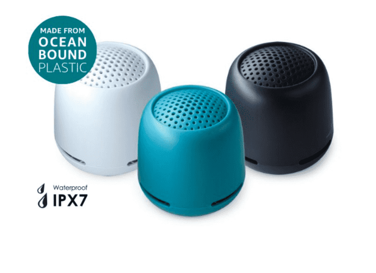Three small, cylindrical portable speakers in white, teal, and black. A badge reads, Made from Ocean Bound Plastic. Text below states, Waterproof IPX7. Each speaker has a perforated top for sound projection.