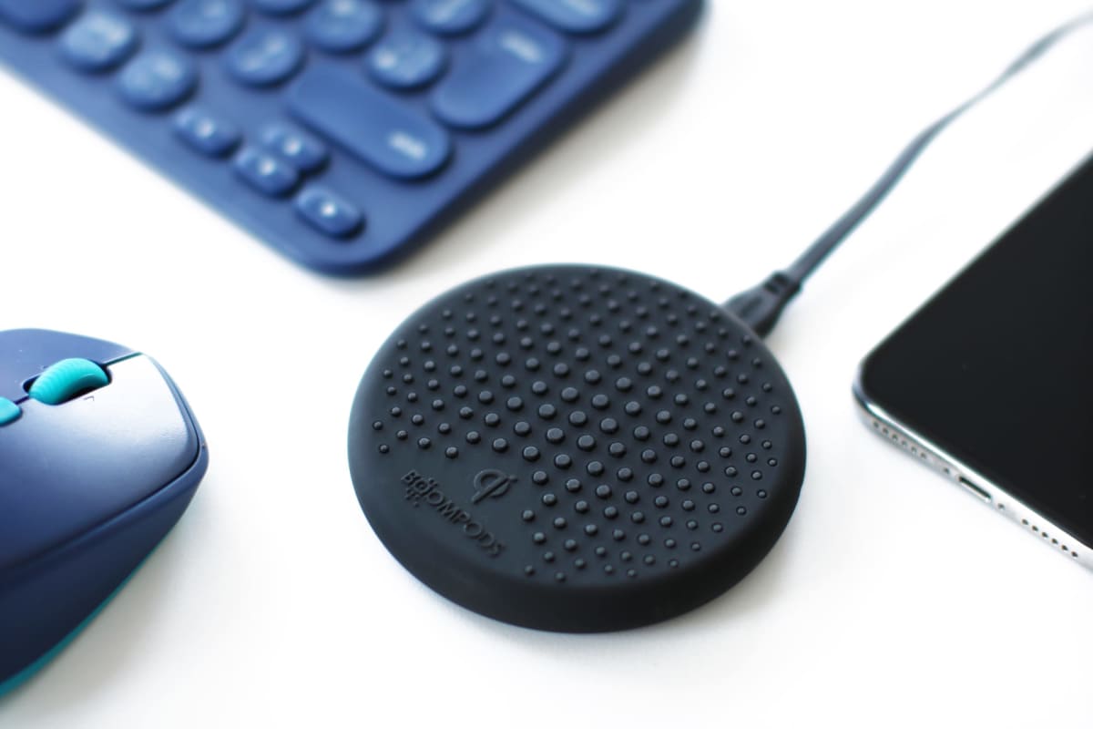 Black wireless charger with textured surface next to a mouse and keyboard.