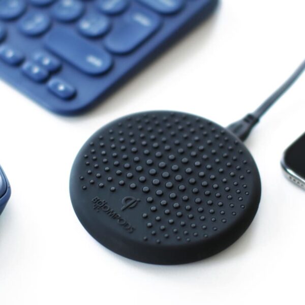 Black wireless charger on desk beside blue mouse, keyboard, and smartphone.