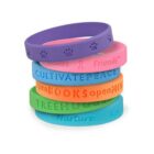 Stack of colorful silicone wristbands with positive words and paw prints.