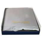A closed gift box with a clear lid, containing a gray item wrapped in tissue paper. The tissue has the words Genuine Leather printed in gold script. The box has a dark base.