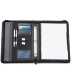 Open black leather portfolio with a spiral notebook on the right. The left side has compartments holding pens, USB drives, a name card, and slots for business cards.