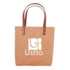 Tan tote bag with brown handles and Usttto logo in white on the front.