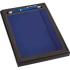 A dark blue notebook with an elastic closure is presented in a black foam-lined box next to a matching blue pen with silver accents. The box has a rectangular shape and provides a snug fit for the notebook and pen.