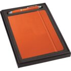An orange notebook with an elastic band and a matching orange pen with silver accents, presented in a black box with foam padding.