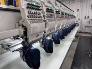 Embroidery machinery in action. A row of caps being decorated with embroidery.