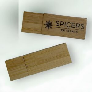 Two bamboo USB flash drives are displayed on a light background. One features SPICERS RETREATS with a star logo, while the other remains plain. Both drives boast a natural wood texture, making them perfect as eco-friendly promotional USBs.