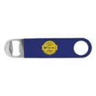 A blue metal bottle opener featuring a round handle hole on one end and a bottle cap opener on the other. In the center, a yellow and black logo reads Cerveza Mexicali de Baja.