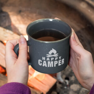 Hands holding a mug with Happy Camper text, near a campfire, surrounded by the cozy vibes of autumn. This favorite autumn scene captures the essence of Shea’s Top 5 seasonal moments.