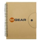 A spiral-bound notebook with a brown kraft paper cover featuring the logo MGEAR in bold black and orange letters. The notebook has a flap with a button closure on the right side.