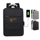 Three backpacks in black and gray are shown. The largest black backpack is labeled Power Office and has a USB charging port connected to a smartphone. The smaller gray and black backpacks are in the background.