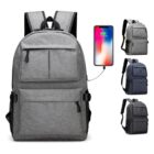 Grey backpack with USB charging port shown alongside a phone, indicating connectivity. Three additional views of similar backpacks in grey and black are displayed to the right.