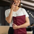 Woman smiling on phone, holding red bag, in a modern office setting.