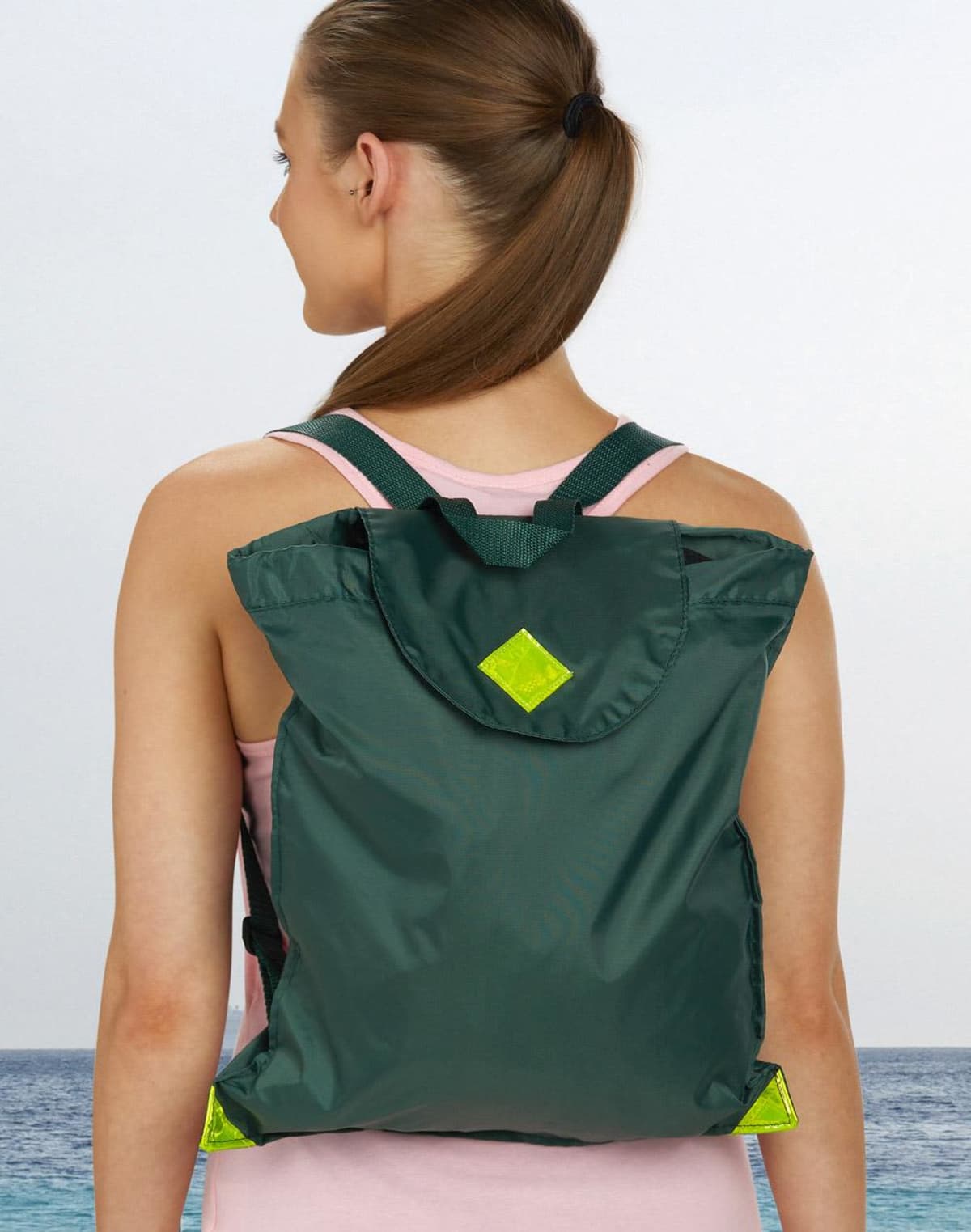 Person with a green backpack stands by the sea, facing away.