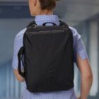 Person in a blue checkered shirt with a black backpack, facing away.