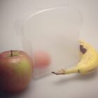 Translucent sandwich container, apple, and a speckled banana on a plain background.