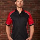 Person in a black and red shirt standing against a brick wall.