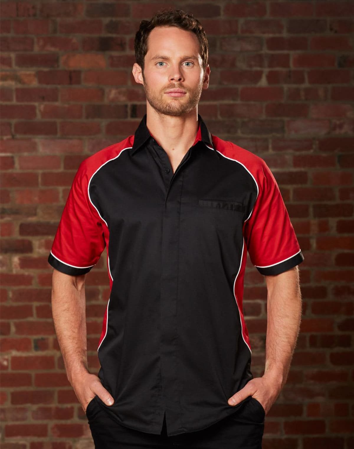Person in a black and red shirt standing against a brick wall.