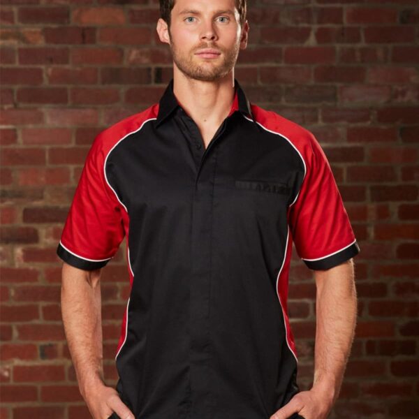 Man in a black and red shirt stands against a brick wall.