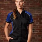 Person in black and blue shirt stands against a brick wall, looking to the side.