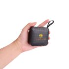 Hand holding a black portable speaker with a logo and wrist strap.