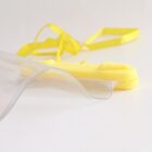 Close-up of a transparent plastic edge with a yellow handle and ribbon on a white surface.