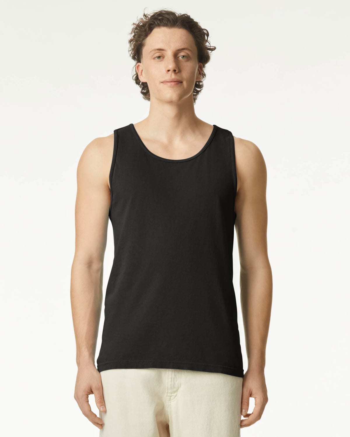 Man wearing a black tank top and light pants, standing against a plain white background.