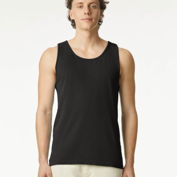 A man wearing a black tank top and light pants standing against a plain white background.