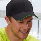 Person in a black cap and green shirt smiling indoors.