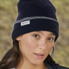 Person wearing a dark knit beanie with a label, against a blurred outdoor background.
