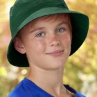 Boy in green hat and blue shirt against a blurred outdoor background.