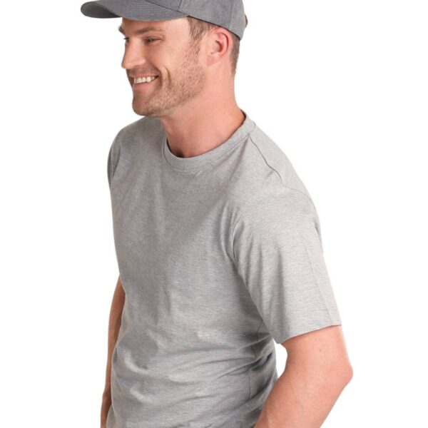 Man wearing a gray t-shirt and cap, smiling with hands in pockets.