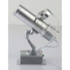Silver LED projector light on a stand, with wires attached, placed on a flat surface.